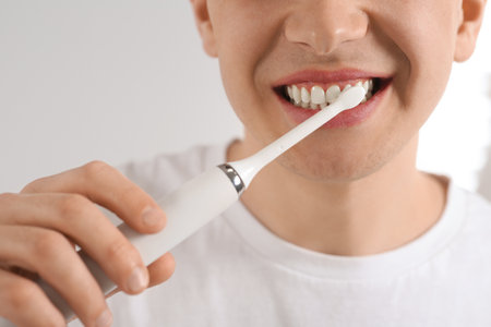Man brushing his teeth with electric toothbrush on blurred background, closeup