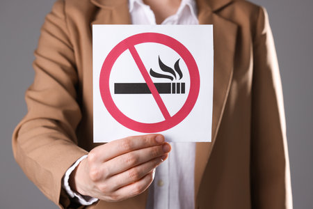 Woman holding card with no smoking sign on gray background, closeupの写真素材
