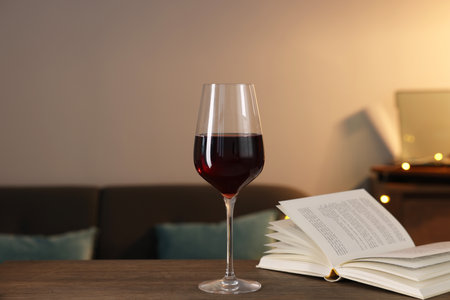 Glass of red wine and open book on wooden table in room. Relax at homeの写真素材