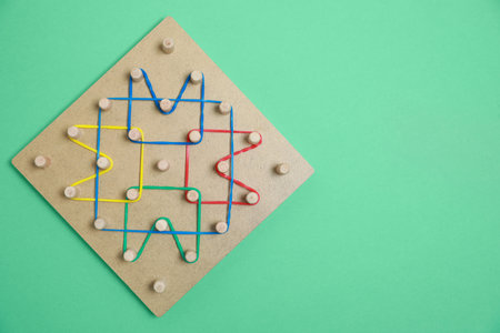 Wooden geoboard with rubber bands on green background, top view with space for text. Educational toy for motor skills developmentの写真素材