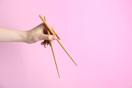 Woman holding pair of wooden chopsticks on pink background, closeup. Space for textの写真素材