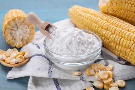 Bowl with corn starch, ripe cobs and kernels on light blue wooden tableの写真素材
