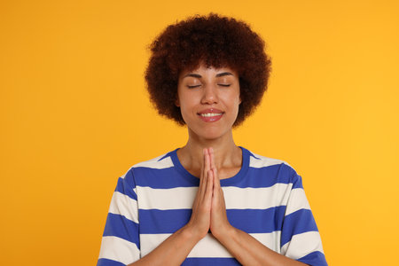 Woman with clasped hands praying to God on orange background
