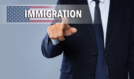 Immigration. Businessman touching digital screen with word and flag of America on gray background, closeupの写真素材