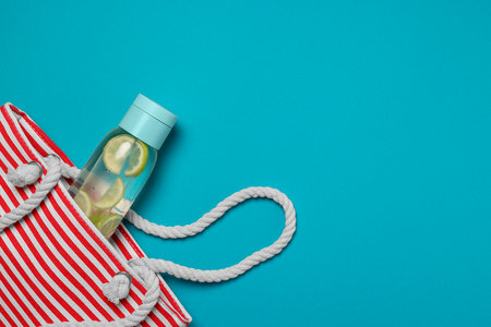 Beach bag and bottle with refreshing drink on light blue background, flat lay. Space for textの写真素材