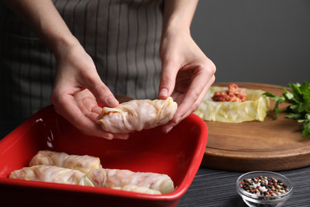 Woman putting uncooked stuffed cabbage roll into baking dish at black table, closeupの写真素材