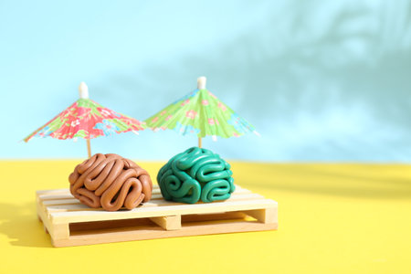 Brains made of plasticine on mini wooden sunbed under umbrellas against color background, space for textの写真素材