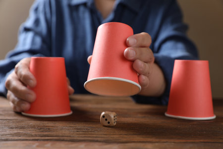 Woman playing thimblerig game with red cups at wooden table, closeupの写真素材