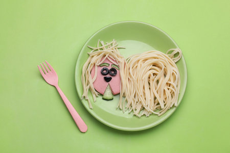 Creative serving for kids. Plate with cute dog made of tasty pasta, sausage and cucumber on green table, flat layの写真素材