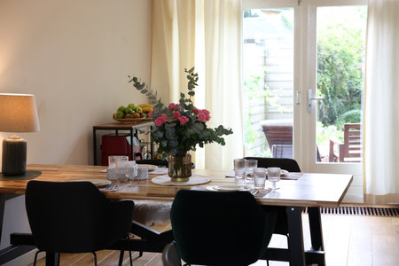 Stylish dining room with comfortable furniture, big window and bouquet of rosesの写真素材