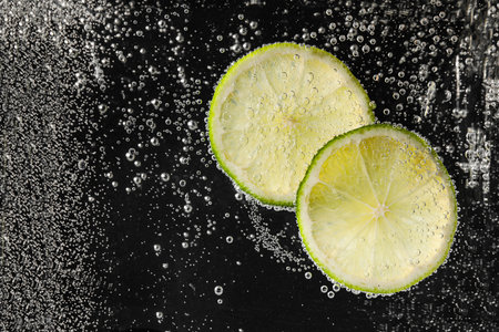 Juicy lime slices in soda water against black background, closeup. Space for textの写真素材