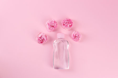 Bottle with baby oil and beautiful flowers on pink background, flat lay. Space for textの写真素材