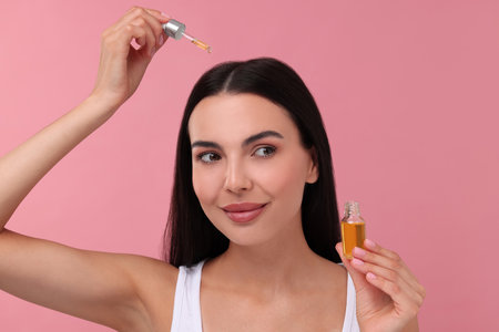 Beautiful woman applying hair serum on pink background. Cosmetic productの写真素材