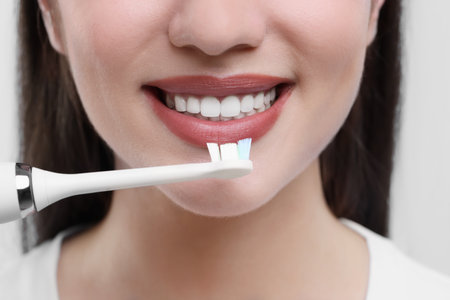 Woman brushing her teeth with electric toothbrush on white background, closeupの写真素材