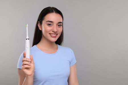 Happy young woman holding electric toothbrush on light gray background, space for textの写真素材