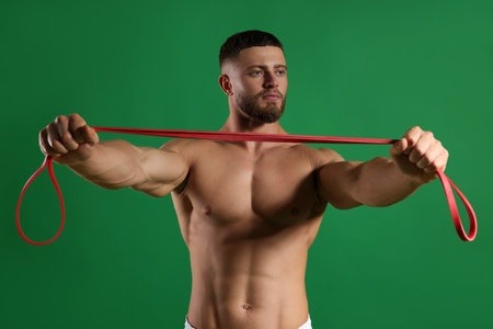 Muscular man exercising with elastic resistance band on green backgroundの写真素材