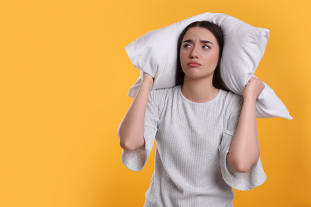 Tired young woman with pillow on yellow background, space for text. Insomnia problemの写真素材