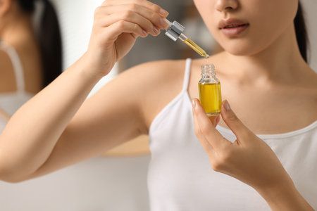 Beautiful young woman with bottle of cosmetic serum in bathroom, closeupの写真素材