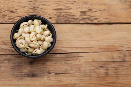 Sprouted kidney beans in bowl on wooden table, top view. Space for text