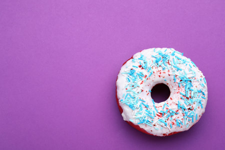 Sweet glazed donut decorated with sprinkles on purple background, top view and space for text. Tasty confectioneryの写真素材
