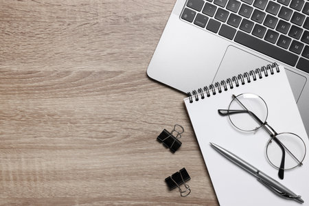 Home office. Laptop, glasses and stationery on wooden desk, flat lay. Space for text
