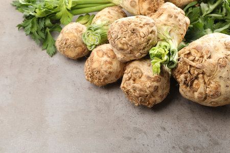 Many raw celery roots and leaves on gray table, space for text