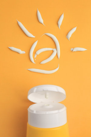 Drawing of sun and tube with sunscreen on orange background, above view. Skin protection