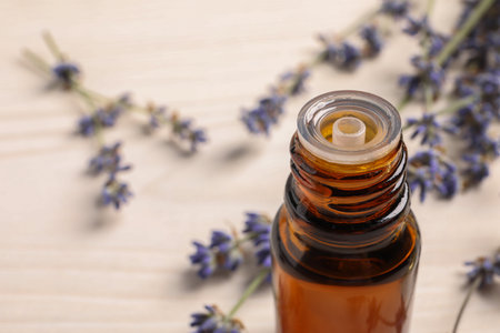 Bottle of essential oil and lavender flowers on white wooden table, closeup. Space for textの写真素材