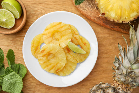 Tasty grilled pineapple slices, fresh lime and mint on wooden table, flat layの写真素材