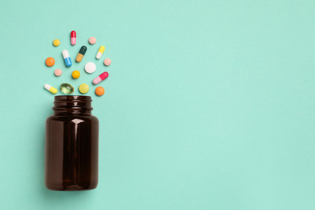 Plastic medical bottle with many different pills on turquoise background, flat lay. Space for text