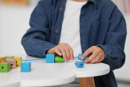 Little boy playing with wooden pieces and string for threading activity at white table indoors, closeup. Child's toyの写真素材