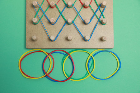 Wooden geoboard with rubber bands on green background, flat lay. Educational toy for motor skills developmentの写真素材