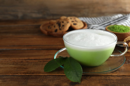 Cup of fresh matcha latte and green leaves on wooden table. Space for textの写真素材