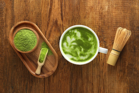 Cup of fresh matcha latte, powder and bamboo whiskey on wooden table, flat layの写真素材
