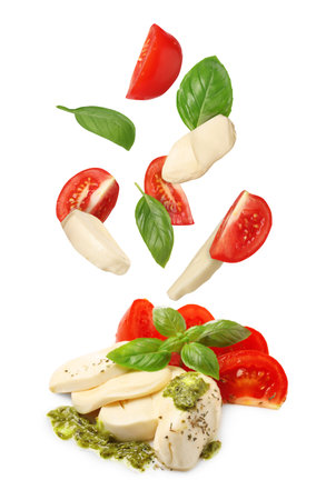 Making Caprese salad. Fresh tomatoes. mozzarella cheese and basil leaves falling against white backgroundの写真素材