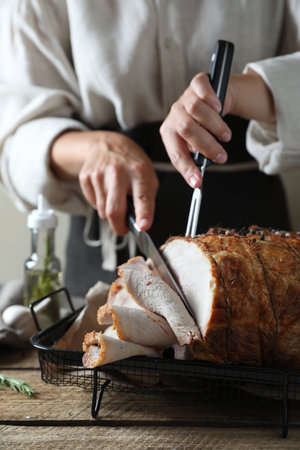 Woman cutting delicious baked ham at wooden table, closeupの写真素材