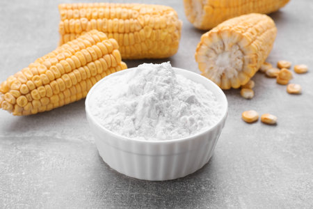Bowl with corn starch and ripe cobs on light gray table, closeupの写真素材
