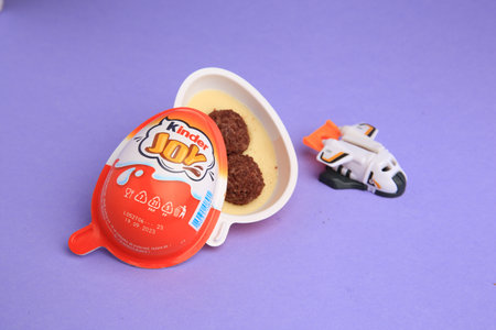Sveti Vlas, Bulgaria - June 30, 2023: Kinder Joy Egg with sweet candies and toy on violet background