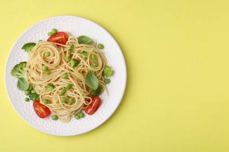 Plate of delicious pasta primavera on yellow background, top view. Space for textの写真素材