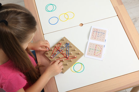 Motor skills development. Girl playing with geoboard and rubber bands at white table, above viewの写真素材