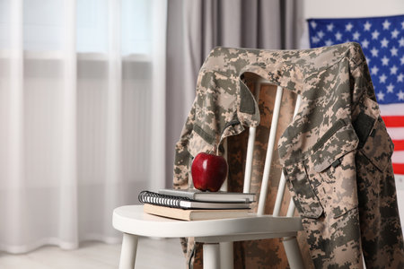 Chair with soldier uniform, notebooks and apple near flag of United States indoors, space for text. Military educationの写真素材