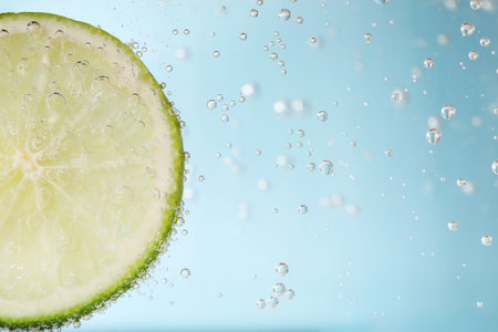 Juicy lime slice in soda water against light blue background, closeup. Space for textの写真素材