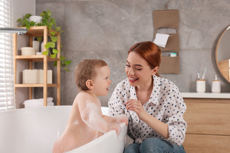 Mother washing her little baby in tub at home
