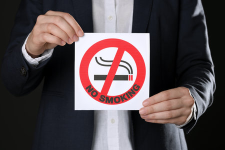 Woman holding card with no smoking sign on black background, closeupの写真素材
