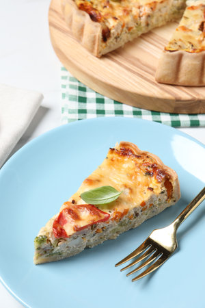 Piece of tasty quiche with chicken, cheese, basil and vegetables on white table, closeupの写真素材