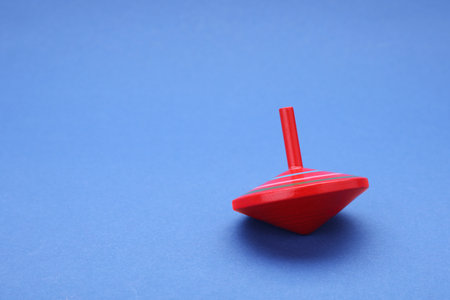 One bright spinning top on blue background, space for text. Toy whirligig