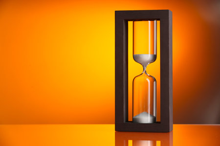 Hourglass with flowing sand on color background. Space for text