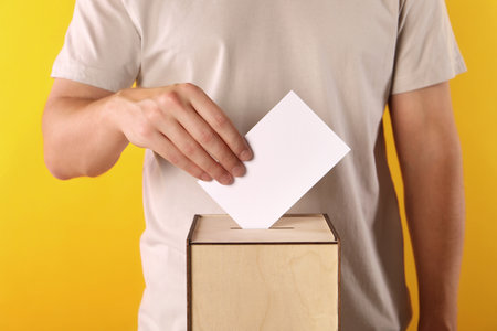 Man putting his vote into ballot box on yellow background, closeupの写真素材