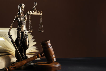 Statue of Lady Justice near gavel and open book on dark table, space for text. Symbol of fair treatment under lawの写真素材