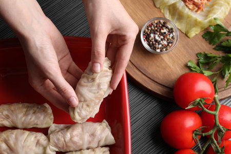 Woman putting uncooked stuffed cabbage roll into baking dish at black table, top viewの写真素材